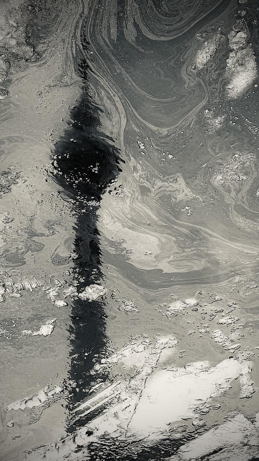 An abstract, monochromatic image featuring swirling dark and light shades, depicting the reflection of a tall structure, likely a tower, in a body of water. The surface displays bubbles and textured patterns.